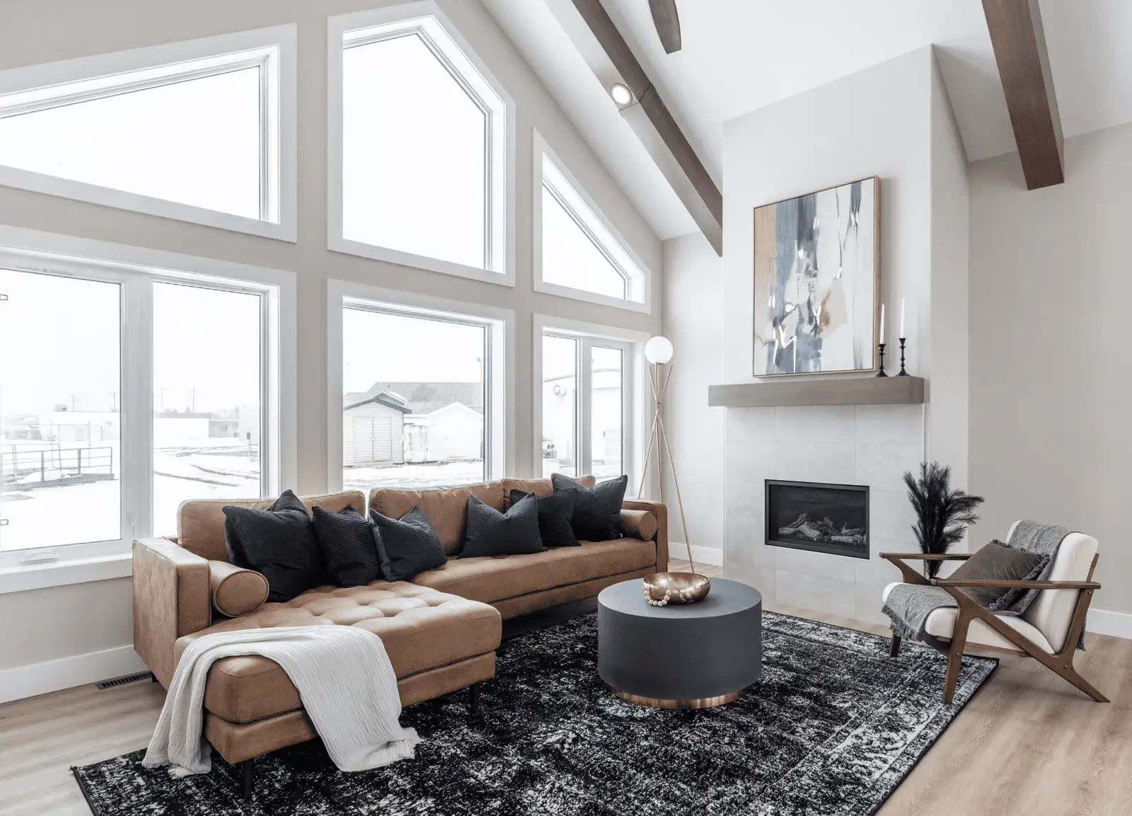 Bright RTM home living room in Alberta or Saskatchewan with vaulted ceiling and triangular windows, tan sectional with dark pillows, round charcoal coffee table, and a modern fireplace with artwork.