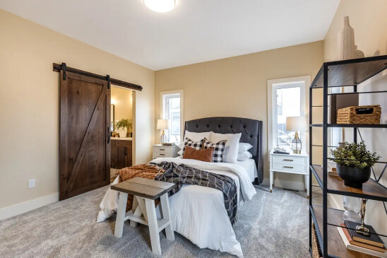 Primary bedroom in a custom RTM home featuring a barn door, large windows, and warm modern finishes.