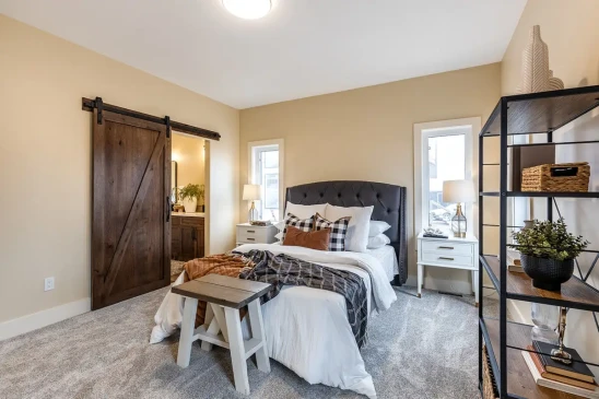 Primary bedroom in a custom RTM home featuring a barn door, large windows, and warm modern finishes.