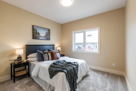 Cozy secondary bedroom in a custom RTM home with large window, soft carpeting, and modern finishes.