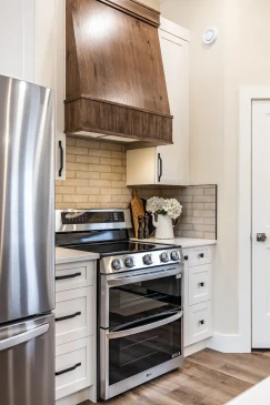 Custom kitchen featuring a decorative wood range hood, white cabinetry, and modern appliances in an RTM home.