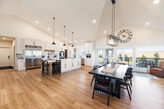 Open concept great room with custom kitchen, dining area, vaulted ceilings, and panoramic backyard views.
