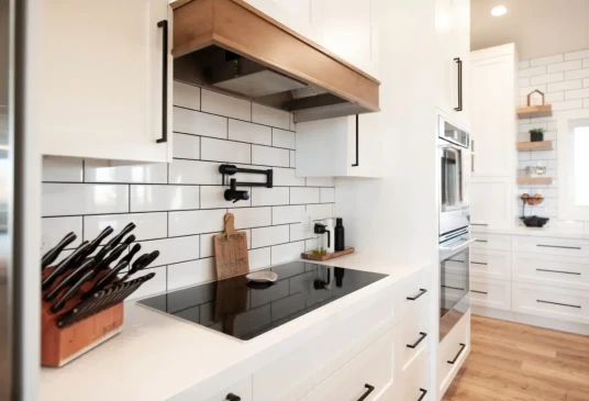 Modern custom kitchen featuring an induction cooktop, pot filler faucet, subway tile backsplash, and white shaker cabinetry.