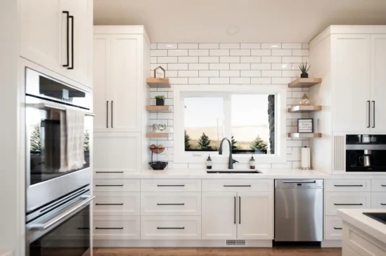 Bright custom kitchen with white shaker cabinets, subway tile backsplash, floating shelves, and stainless steel appliances.