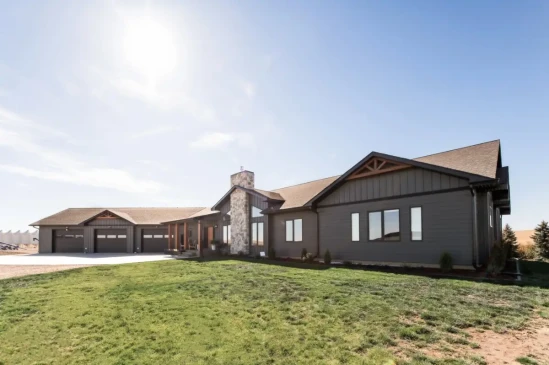 Modern custom home with dark siding, stone accents, covered front porch, and landscaped yard.