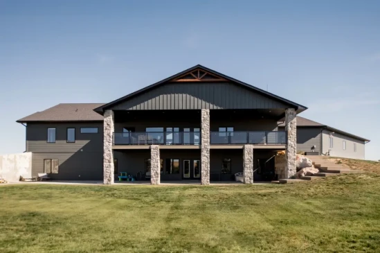 Rear view of a custom luxury home featuring a covered deck, walkout basement, and stone columns.