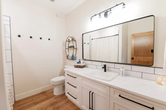 Modern guest bathroom with white shaker vanity, large mirror, subway tile, and black hardware.