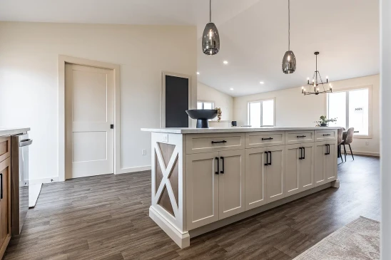 Spacious modern kitchen with a large white island featuring wood accents, black hardware, and pendant lighting, opening into a bright dining area with large windows and contemporary chandelier.