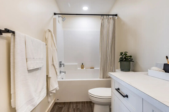Contemporary bathroom in a ready-to-move home featuring a white bathtub and shower combo with a striped curtain, modern vanity with white countertop, towel rack, and potted plant accent.