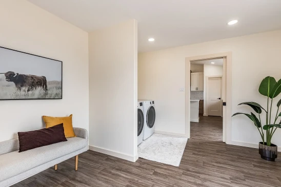 Modern laundry room in a ready-to-move home featuring front-load washer and dryer, wood-style flooring, minimalist decor, and a cozy bench with accent pillows.