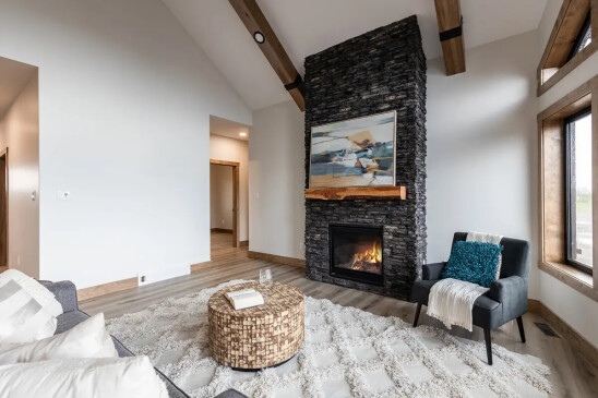 Open concept living room in RTM home featuring floor-to-ceiling stone fireplace and exposed wood beams in Alberta and Saskatchewan