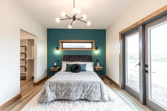 Modern primary bedroom in RTM home with vaulted ceiling, teal accent wall and patio doors, ready-to-move home in Alberta and Saskatchewan