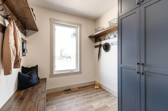 Bright mudroom with navy blue cabinets, wooden bench, coat hooks, and shelving with storage baskets.