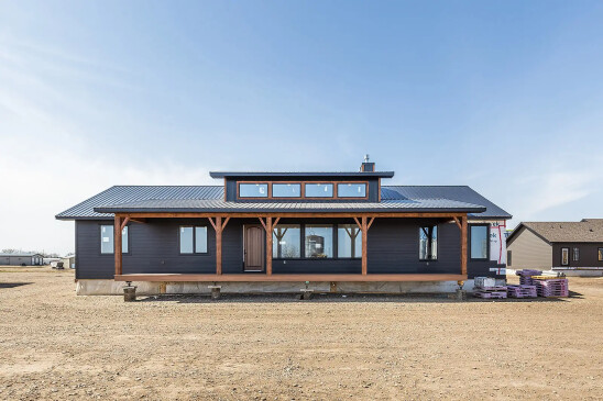Modern RTM home with dark siding, wood posts, metal roof, and a covered front porch featuring large windows and clerestory accents for natural light.