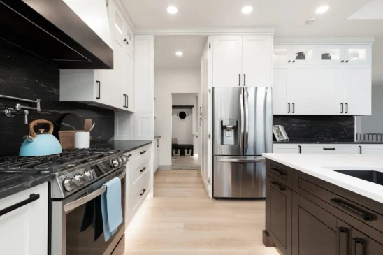 Bright custom kitchen with white cabinetry, black backsplash, quartz countertops, and stainless steel appliances.