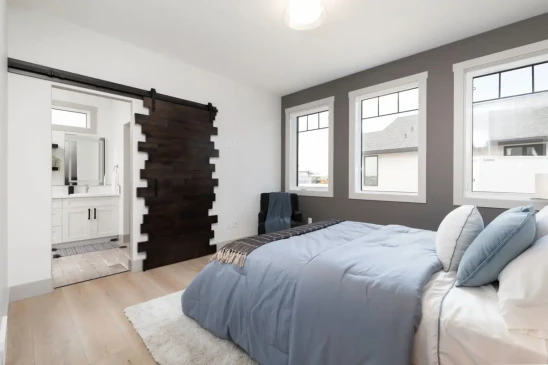 Bright primary bedroom in a custom RTM home with sliding barn door and contemporary finishes.
