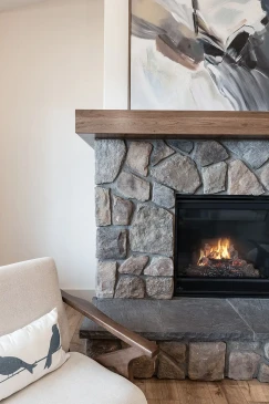 Natural stone fireplace surround with dark hearth and wood mantel in modern RTM home